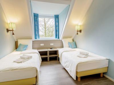 Licht ingericht tweepersoonskamer met twee eenpersoonsbedden en groot raam