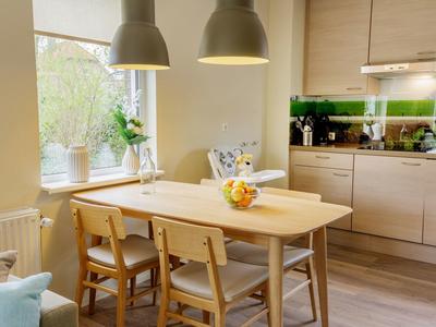 Lichte keuken- en eetruimte met houten meubels en grote ramen die daglicht binnenlaten.