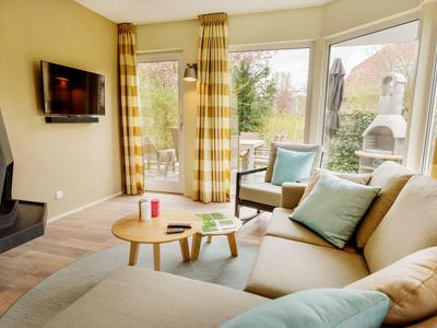 Gezellige woonkamer met hoekbank, open haard, tv en grote ramen met uitzicht op de tuin.