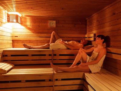 Twee vrouwen ontspannen in een sauna met houten banken en gedimd licht.