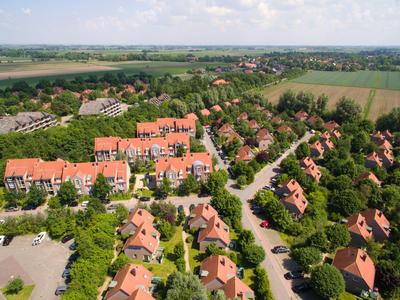 Luchtfoto van een vakantiepark met rode daken, omgeven door groene velden en bomen.