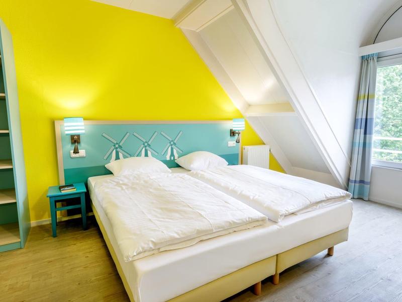 Felgeel hotelkamer met twee bedden onder een schuine plafond en groot raam