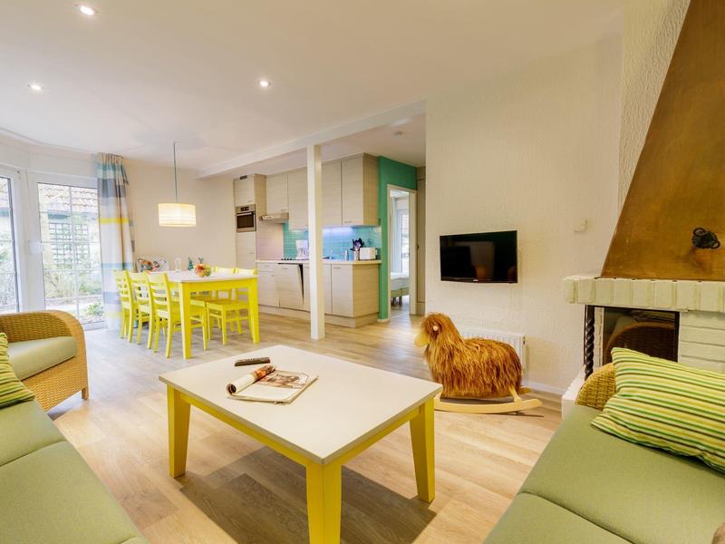 Lichte woonkamer met groene banken, gele tafel en moderne keuken op de achtergrond.