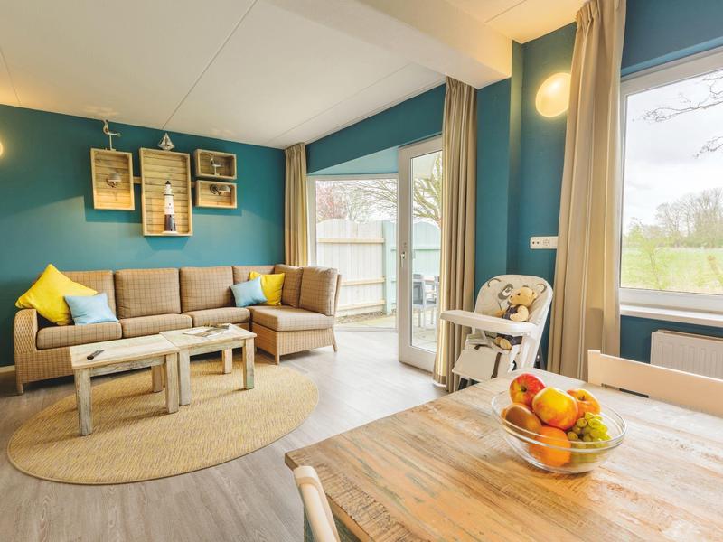 Lichte woonkamer met blauwe accentmuur, bank, salontafel en toegang tot terras.