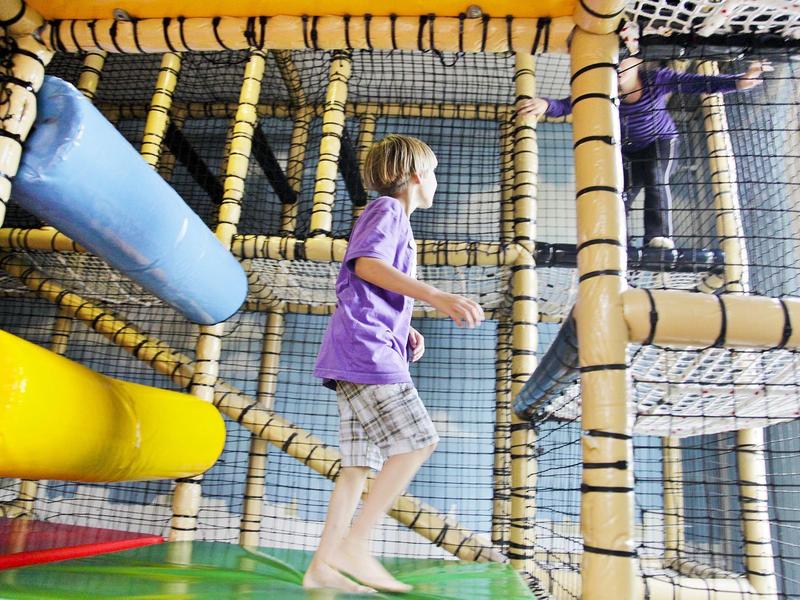 Kind speelt in kleurrijke indoor speeltuin met glijbanen en klimstructuur.