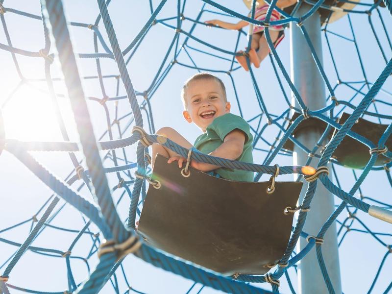 Kinderen schommelen op een touwen klimrek bij zonnig weer.