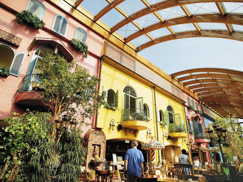 Kleurrijke rij huizen onder grote glazen overkapping met planten en een voorbijganger