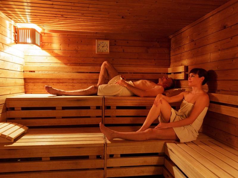 Twee vrouwen ontspannen in een sauna met houten banken en gedimd licht.