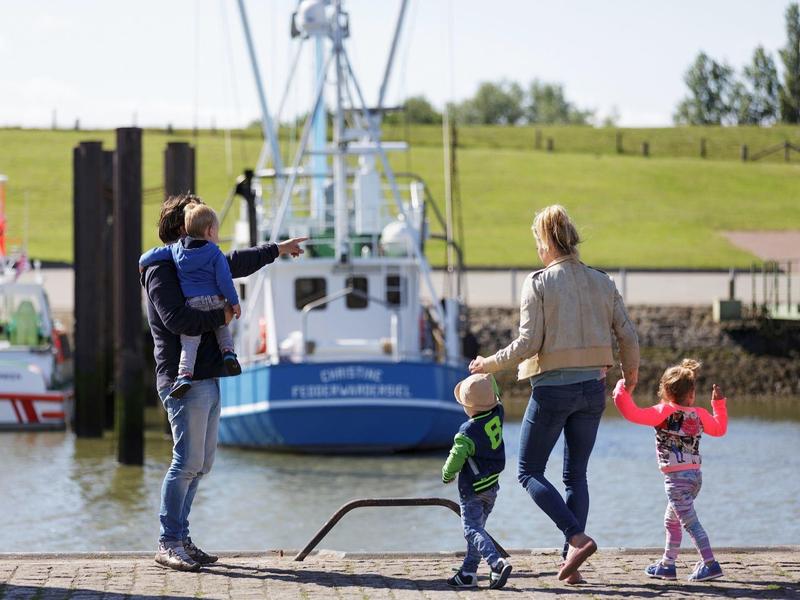 Gezin met twee kinderen wandelen langs het water met boten op de achtergrond.