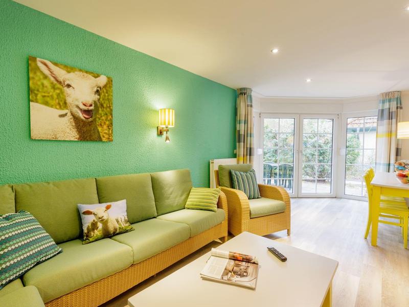 Lichte woonkamer met groene muur, groene bank en groot raam met uitzicht op tuin.