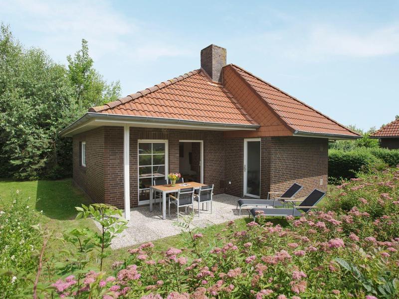 Kleine vakantiewoning met terras en tuin, omgeven door bloemen en struiken.
