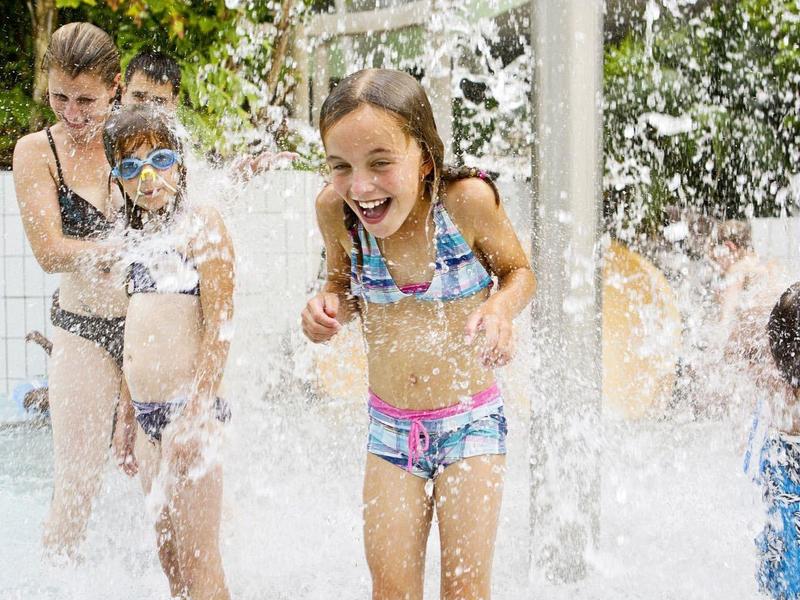 Des enfants rient en jouant sous des jets d'eau à l'extérieur.