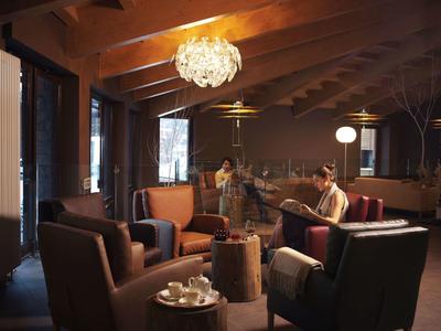 Gemütliches Wohnzimmer mit dunklen Ledersesseln, Holzdecke und zwei Personen beim Lesen.