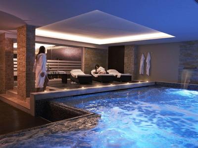 Innenbereich mit beleuchtetem Schwimmbecken, Liegen und entspannter Atmosphäre in warmem Licht.