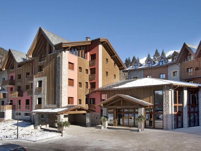 Mehrstöckige Unterkunft mit spitzen Dächern, hellem Himmel und schneefreiem Asphaltbereich.