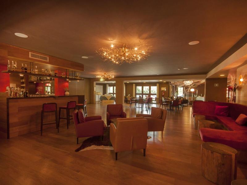 Gemütliche Hotelbar mit Holzboden, roten Sesseln, Holztheke und warmem Deckenlicht.