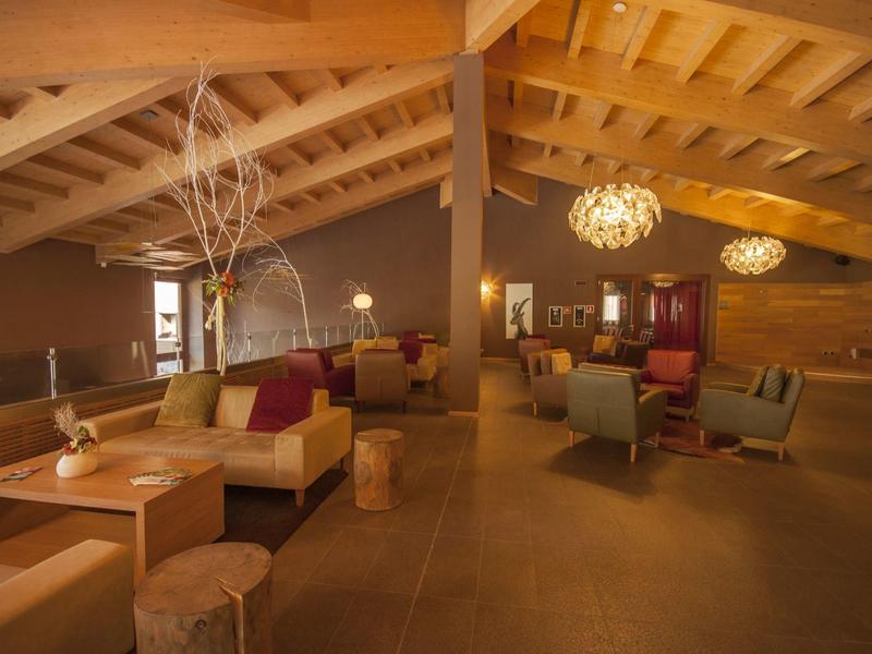 Gemütlicher Gastraum mit Holzbalkendecke, warmem Licht und Sitzgruppen aus Holz und Polsterstühlen.