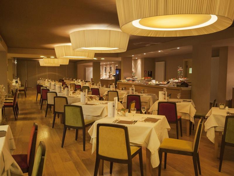 Weitläufiges Restaurant mit gedeckten Tischen, gepolsterten Stühlen und warmem, gelbem Licht.