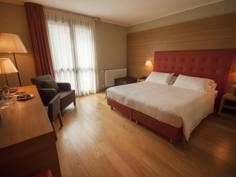 Gemütliches Hotelzimmer mit Doppelbett, Schreibtisch, zwei Sesseln und warmem Licht.