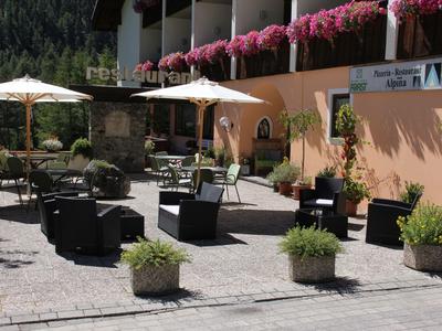 Terrasse mit Sitzgruppen, Sonnenschirmen und Pflanzen vor einem Hotelgebäude mit Blumen am Balkon.