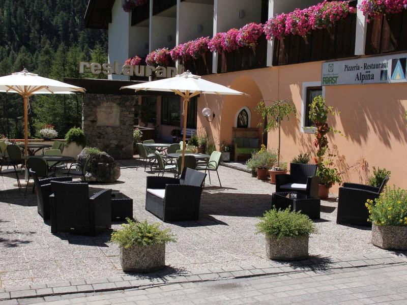 Außenbereich mit Sitzgruppen, Schirmen und Pflanzen vor einem Blumen-geschmückten Gebäude.