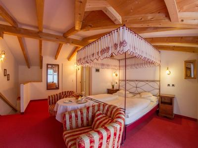 Gemütliches Hotelzimmer mit Himmelbett, roten Teppichboden und gepolstertem Sessel.