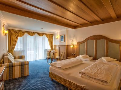 Gemütliches Hotelzimmer mit Doppelbett, Holzdecke, blauem Teppich und Fenster mit gelben Vorhängen.