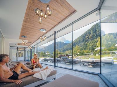 Modernes Wohnzimmer mit großen Glasfenstern und Blick auf grüne Berge und blauen Himmel.
