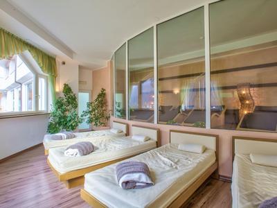 Raum mit großen Fenstern, drei Einzelbetten mit weißen Laken und Handtüchern, hölzerner Boden.