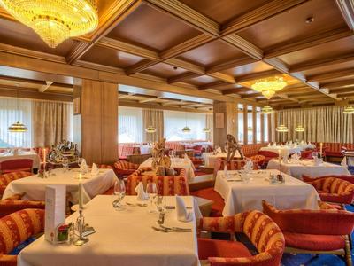 Großes Restaurant mit Holzdecke, roten Sesseln, weißen Tischtüchern und warmem Deckenlicht.