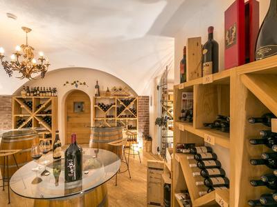 Weinkeller mit Holzmöbeln, Regalen voller Weinflaschen und einem runden Glastisch in warmem Licht.