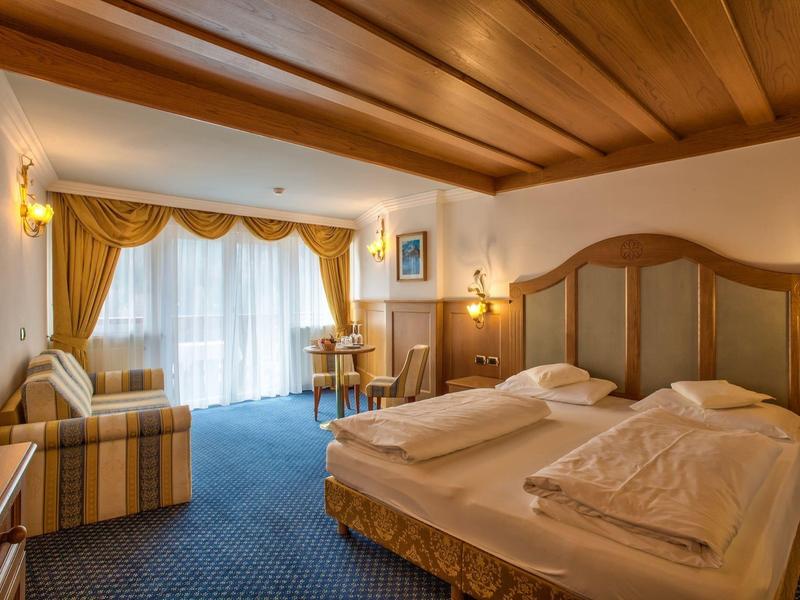 Gemütliches Hotelzimmer mit Doppelbett, Holzdecke, blauem Teppich und Fenster mit gelben Vorhängen.