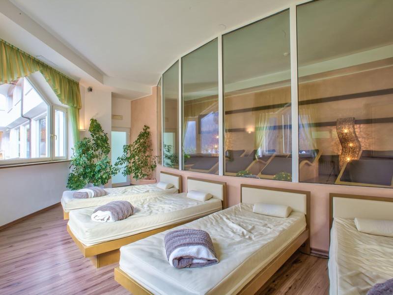 Raum mit großen Fenstern, drei Einzelbetten mit weißen Laken und Handtüchern, hölzerner Boden.