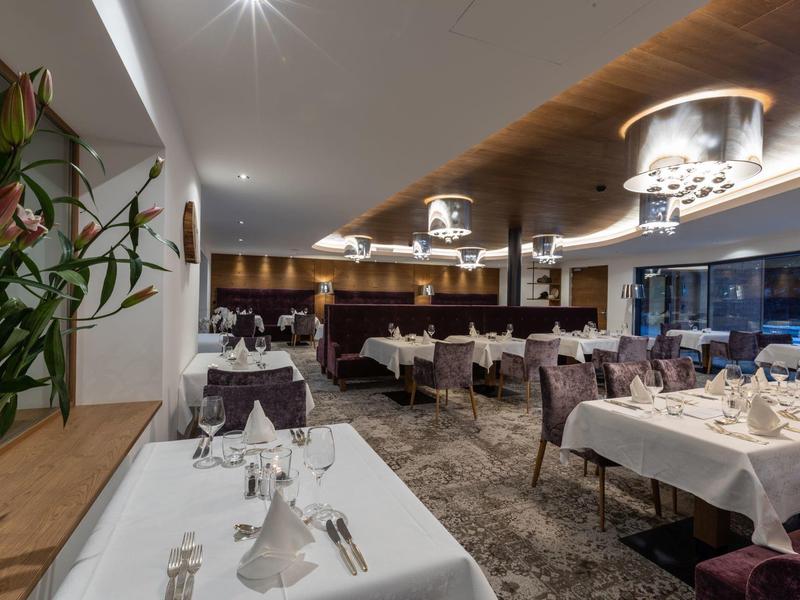 Elegantes Restaurant mit gedeckten Tischen, violetten Stühlen und moderner Deckenbeleuchtung.
