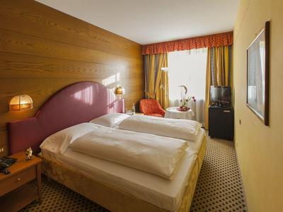 Gemütliches Schlafzimmer mit großem Bett, Holzwand, gelben Wänden und Teppichboden.