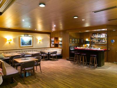 Gemütliche Bar mit Holzmöbeln, Theke, Hockern, Sitzgruppen und warmem Licht.