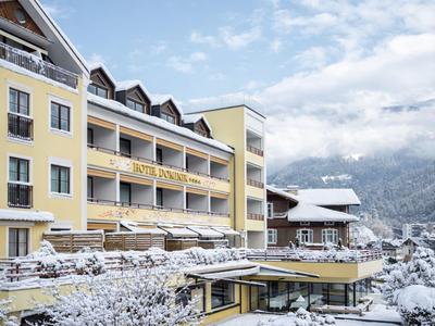 Gelbes Hotelgebäude in verschneiter Berglandschaft mit Bäumen und Terrasse.