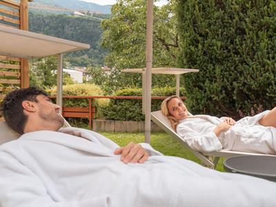Zwei entspannte Personen in Bademänteln liegen im Garten eines Hotels.