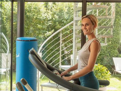 Frau läuft auf einem Laufband vor großen Fenstern mit Blick auf einen Garten.