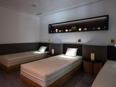 Drei Einzelbetten mit weißen Bettlaken in einem minimalistischen Hotelzimmer mit indirekter Beleuchtung.