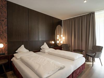 Modernes Hotelzimmer mit zwei Einzelbetten, dunkler Holzverkleidung und stilvoller Beleuchtung.