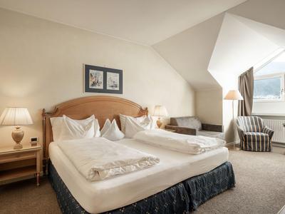 Ein gepflegtes Hotelzimmer mit zwei Einzelbetten, Nachttischen, Lampen und einem Sitzbereich mit Fensterblick.