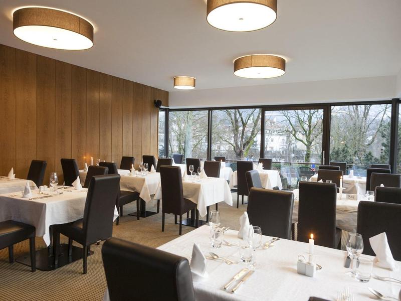 Modernes Restaurant mit brauner Holzwand, großen Fenstern und weißen gedeckten Tischen.