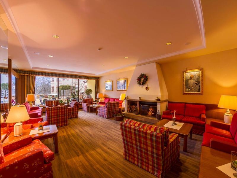 Gemütliches Wohnzimmer mit Kamin, roten Sesseln, Teppichboden und warmem Licht in warmen Farben.