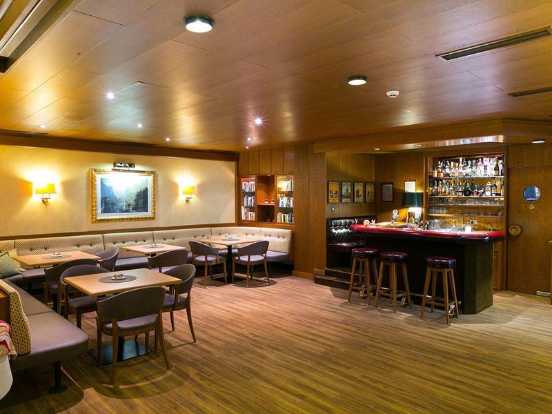 Gemütliche Bar mit Holzmöbeln, Theke, Hockern, Sitzgruppen und warmem Licht.