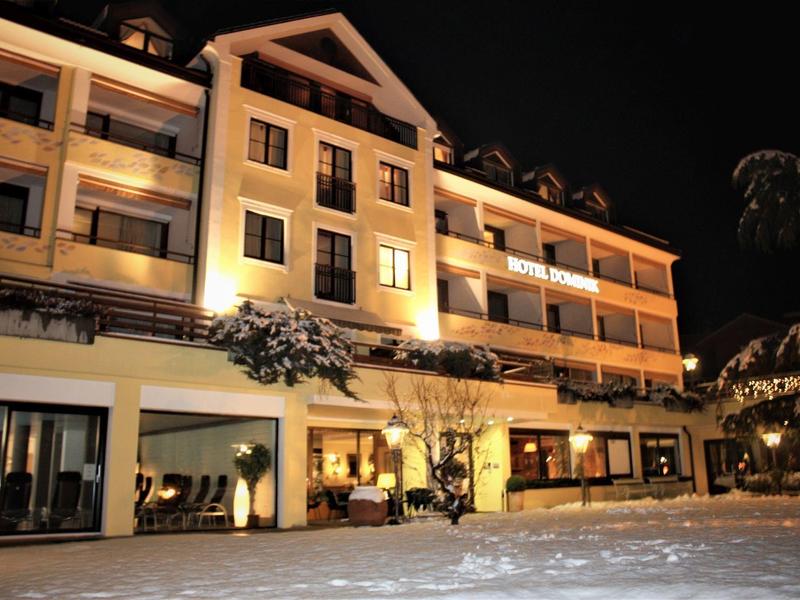 Beleuchtetes Hotelgebäude mit Balkonen und Schnee im Vordergrund bei Nacht.