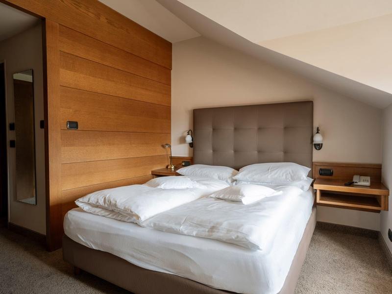 Hell gestaltetes Schlafzimmer mit Doppelbett, Holzwand, grauem Kopfteil und eingebauten Nachttischen.