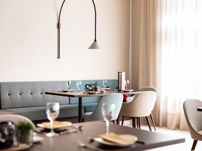 Área de comedor moderna con mesa, sillas y ventanas grandes que permiten luz natural en una habitación de hotel.