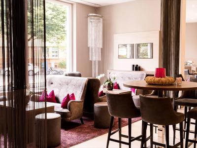 Gemütliches Wohnzimmer mit beigen Wänden, Holzmöbeln, rotem Teppich und großen Fenstern.