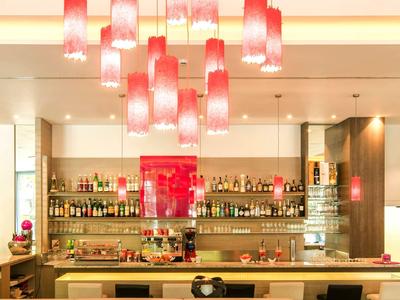 Moderner Barbereich mit hellroten Hängelampen, großem Regal voller Flaschen und hellem Tresen.